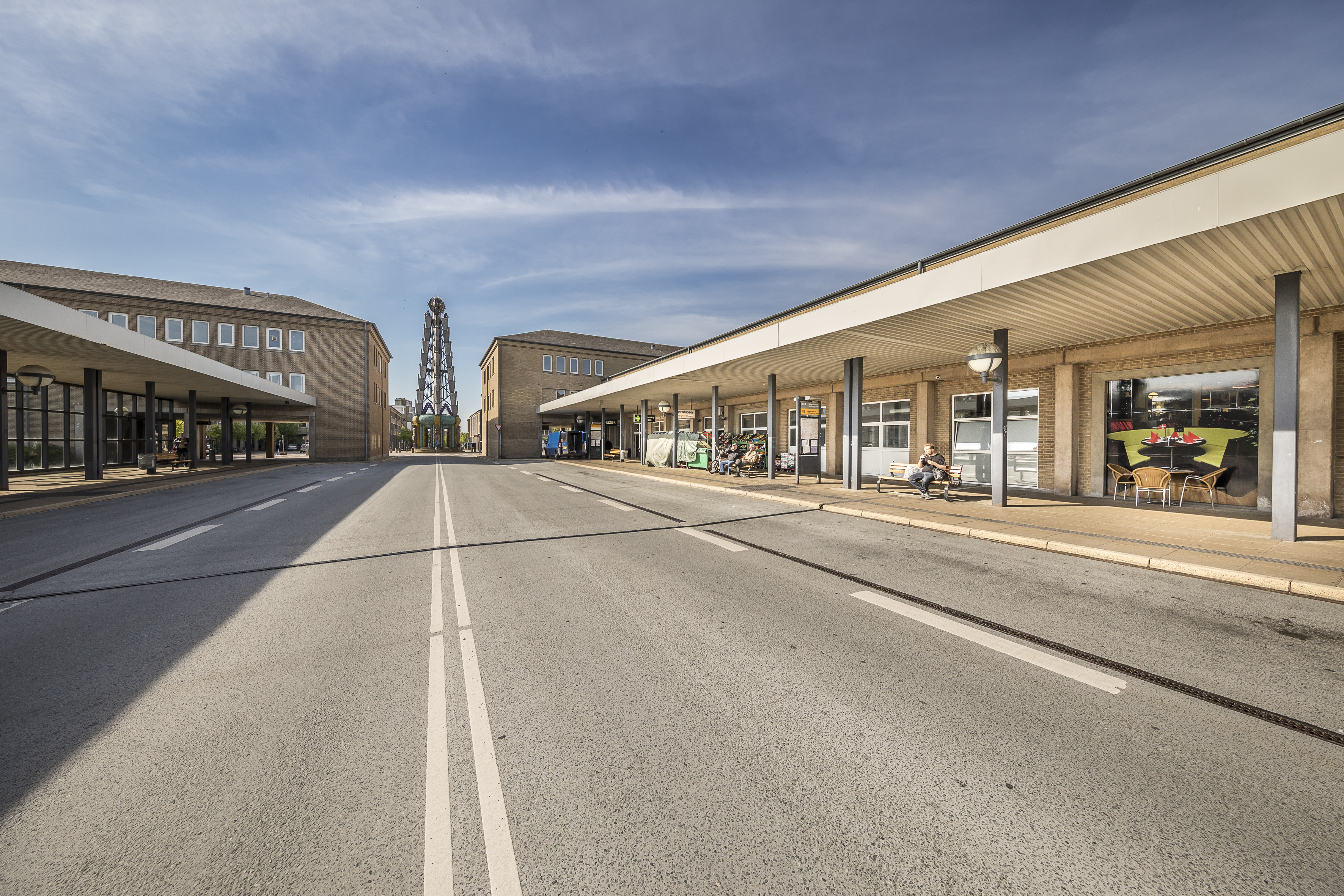 Et menneske der venter på bussen ved busholdepladsen ved Banestrøget 7 på en solskinsdag